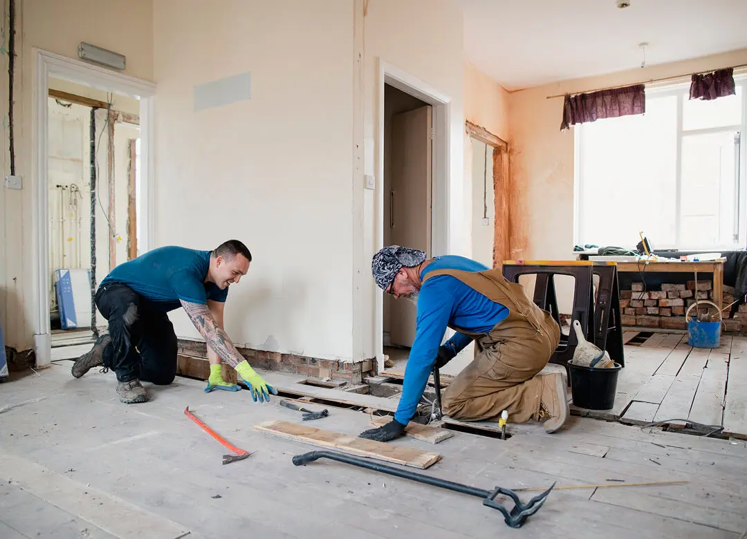 Two workers renovating a room floor.