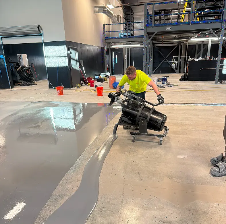 Worker smoothing concrete floor in industrial space.